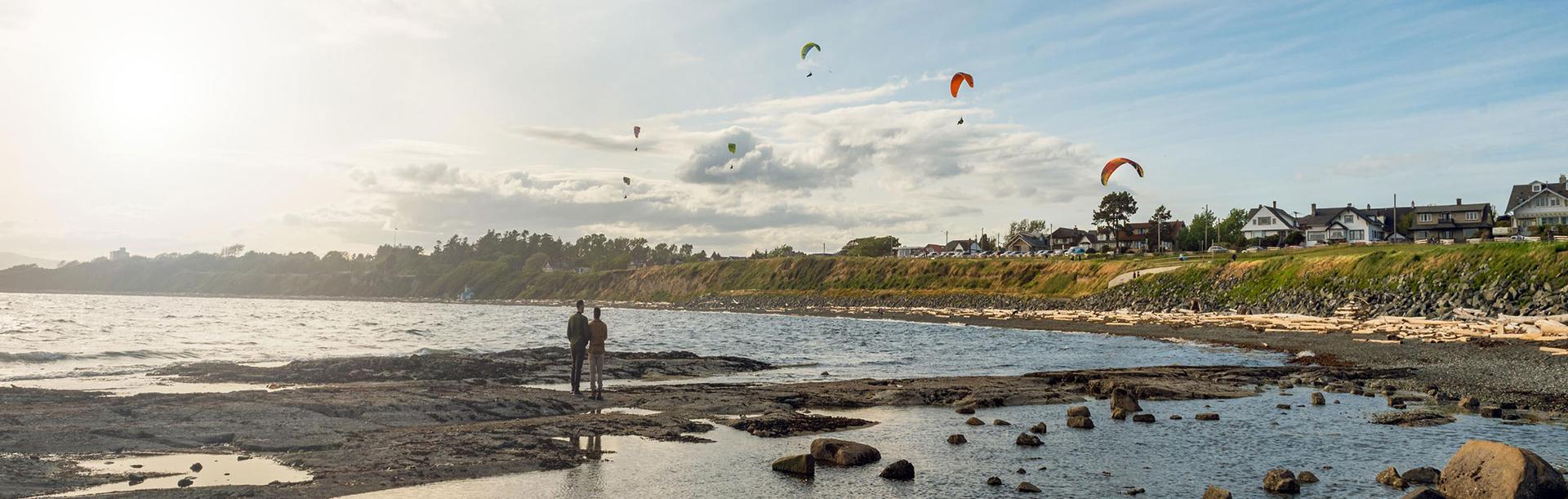 A couple watches the parasailers above Dallas Road Beach from Clover Point in Victoria, BC
