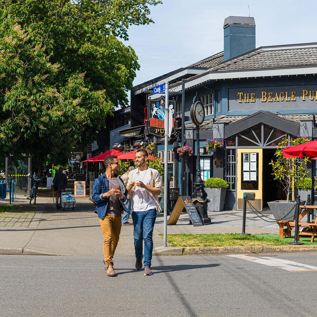 A male couple walks through Cook Street Village eating ice cream in Victoria, BC