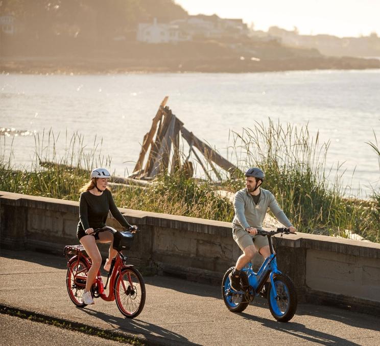A couple rides red and blue e-bikes along an oceanfront pathway in Victoria, BC's Fairfield neighbourhood