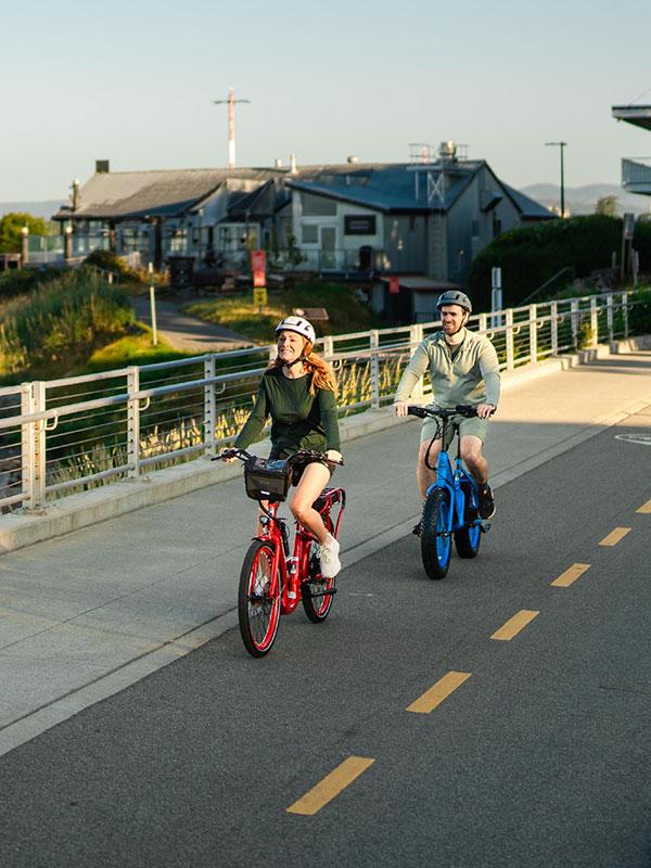 A couple rides bikes along the waterfront on the Dallas Road bike path in the James Bay neighbourhood of Victoria, BC at sunset