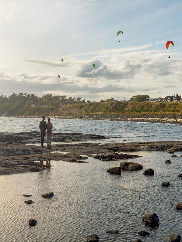 A couple watches the paragliders from the beach at Clover Point in Victoria, BC's Fairfield neighbourhood