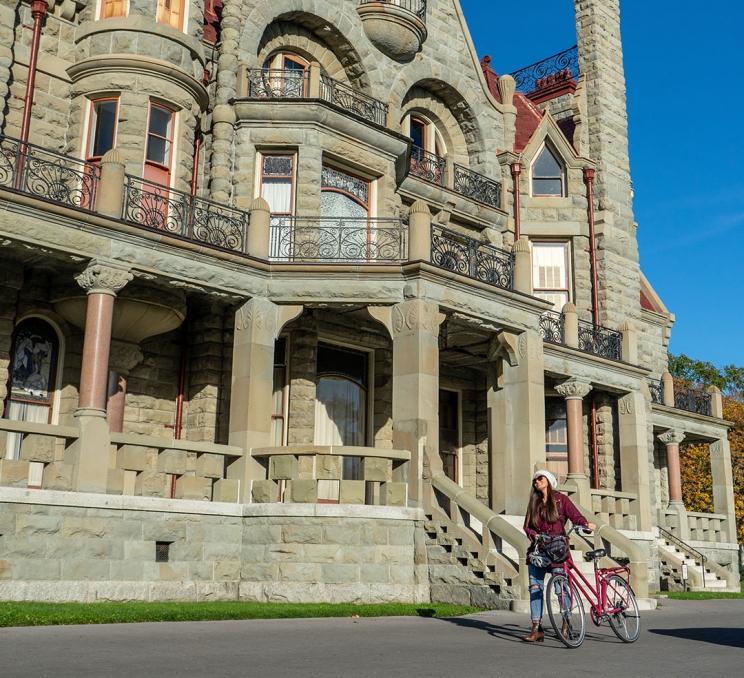 A woman pushes her bike past Craigdarroch Castle Historic House & Museum in Victoria, BC's Rockland neighbourhood