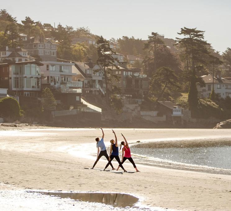 A group of three women practice morning yoga on Gonzales Beach in Victoria, BC