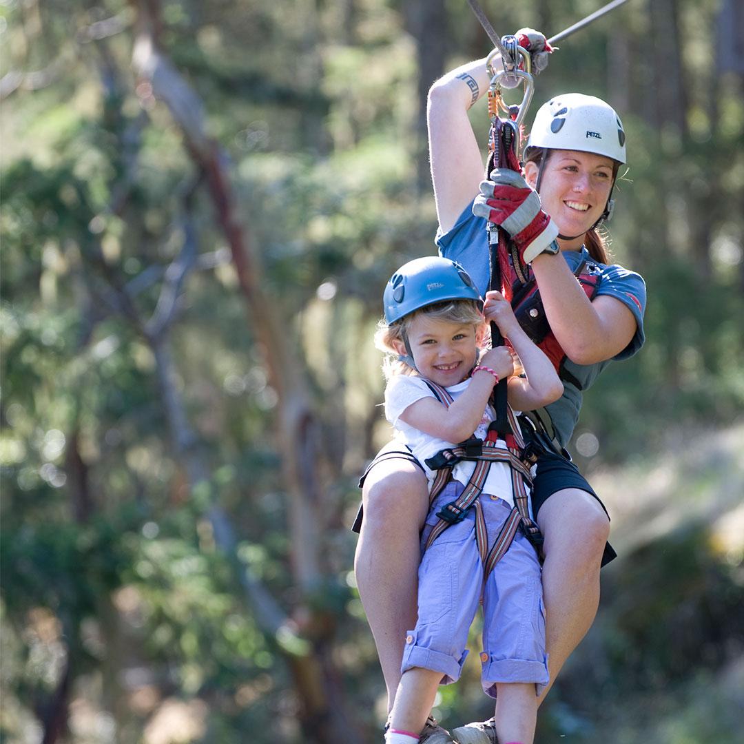 A mother and daughter ride a zipline through the trees