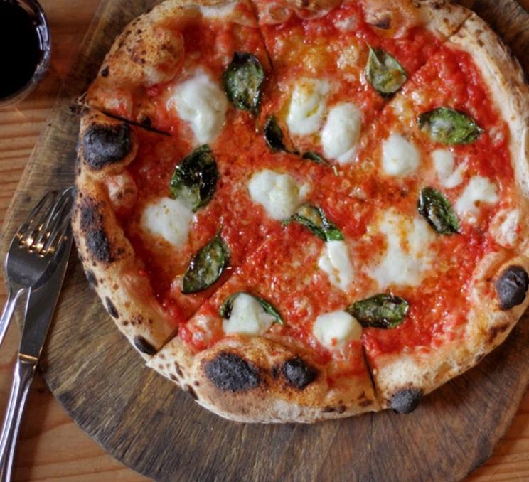 A pizza with mozzarella and basil rests on a cutting board