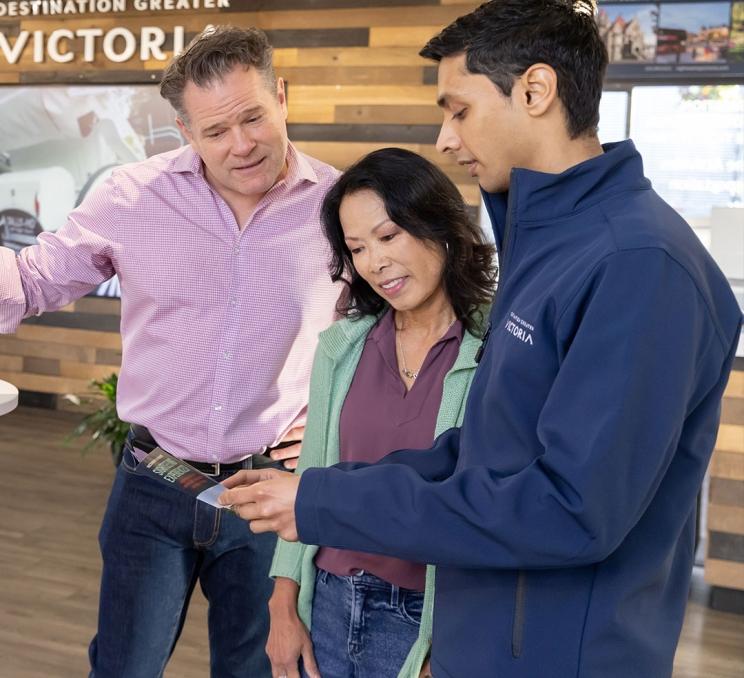 A Destination Greater Victoria Visitor Centre employee shows a couple of visitors a brochure inside the Victoria Visitor Centre in Victoria, BC
