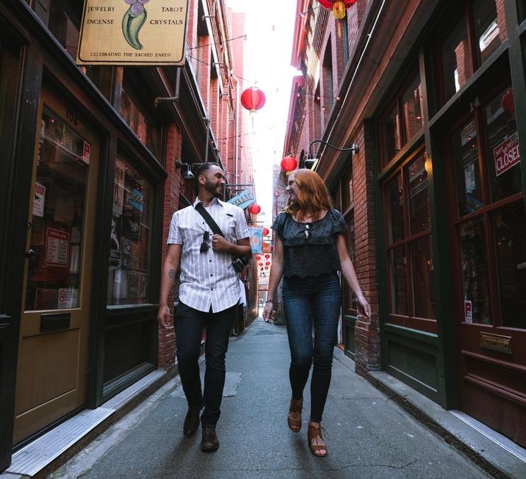 A man in a white collared shirt walks with a woman in blue down Fan Tan alley, Canada's narrowest street, in Victoria, BC