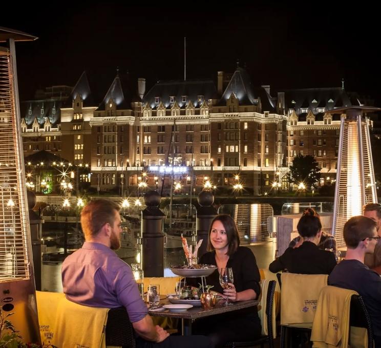A couple dines on a Seafood Tower, backdropped by the Fairmont Empress Hotel, at the Steamship Grill & in Victoria, BC