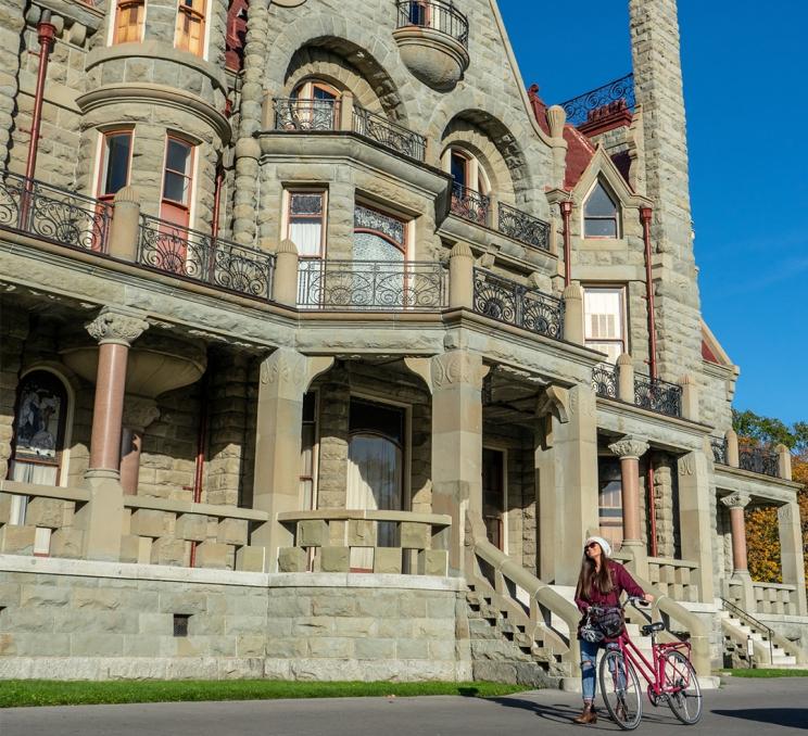 A woman pushes her bike in front of Craigdarroch Castle in Victoria, BC