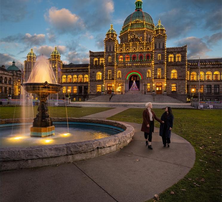 A couple walks together past a fountain at the BC Parliament Buildings in Victoria, BC