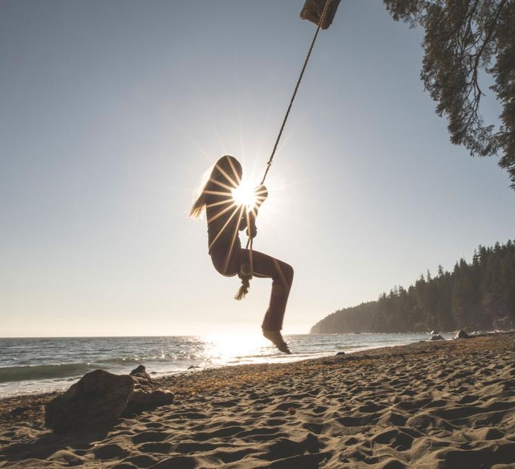 A woman swings on a rope swing on a beach in Greater Victoria, BC at sunset