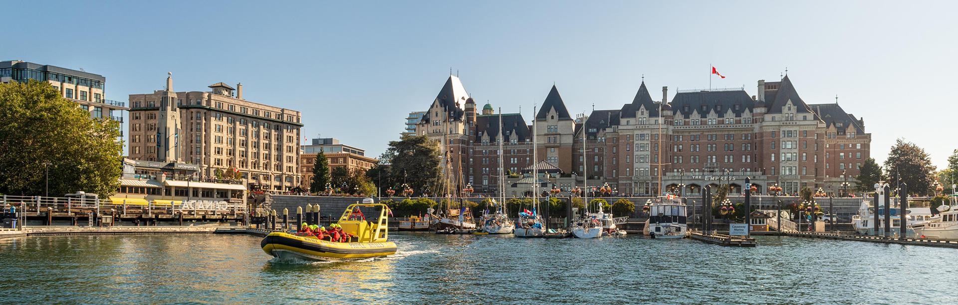 A yellow zodiac boat departs the Inner Harbour for a whale watching tour with the Fairmont Empress in the background in Victoria, BC