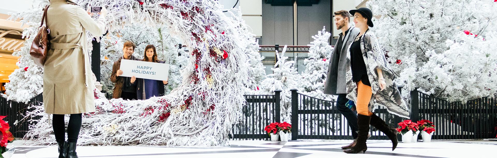 A couple walks through a holiday display while a couple has their photo take in the Bay Centre Shopping Centre in Victoria, BC