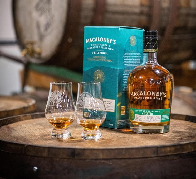 Two drams of Macaloney's Island Distiller's whiskey stand alongside a bottle on top of a barrel in Victoria, BC