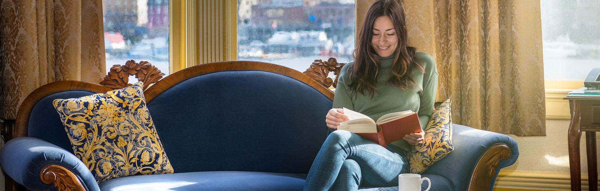A woman reads a book while sitting on a sofa at a hotel in Victoria, BC