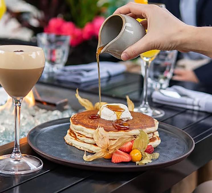 Stack of fluffy pancakes topped with whipped cream and maple syrup at Fathom Restaurant in Victoria, BC