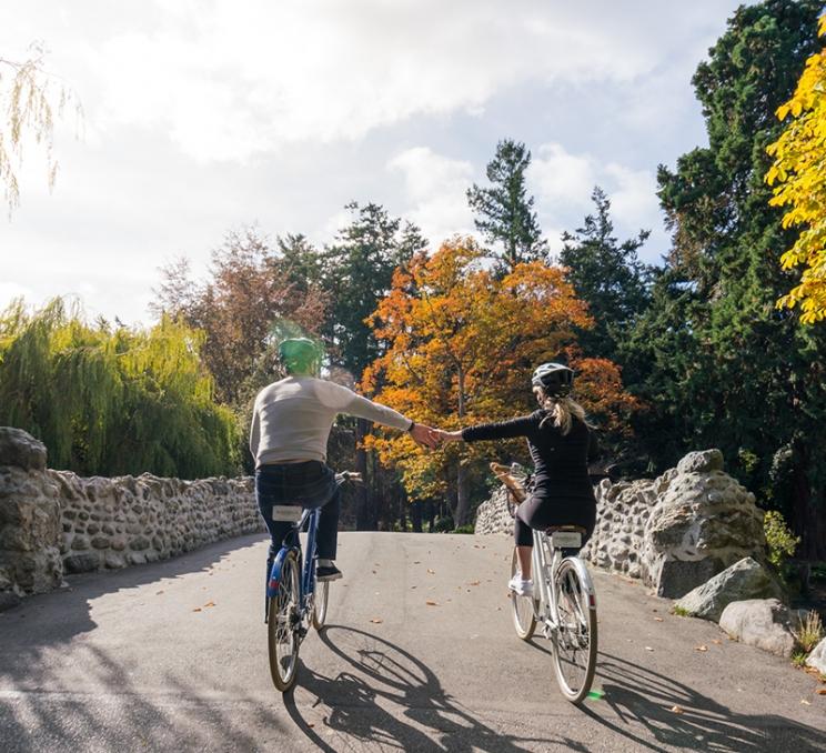 Cyclists ride hand-in-hand across the stone bridge in Beacon Hill Park in Victoria, BC