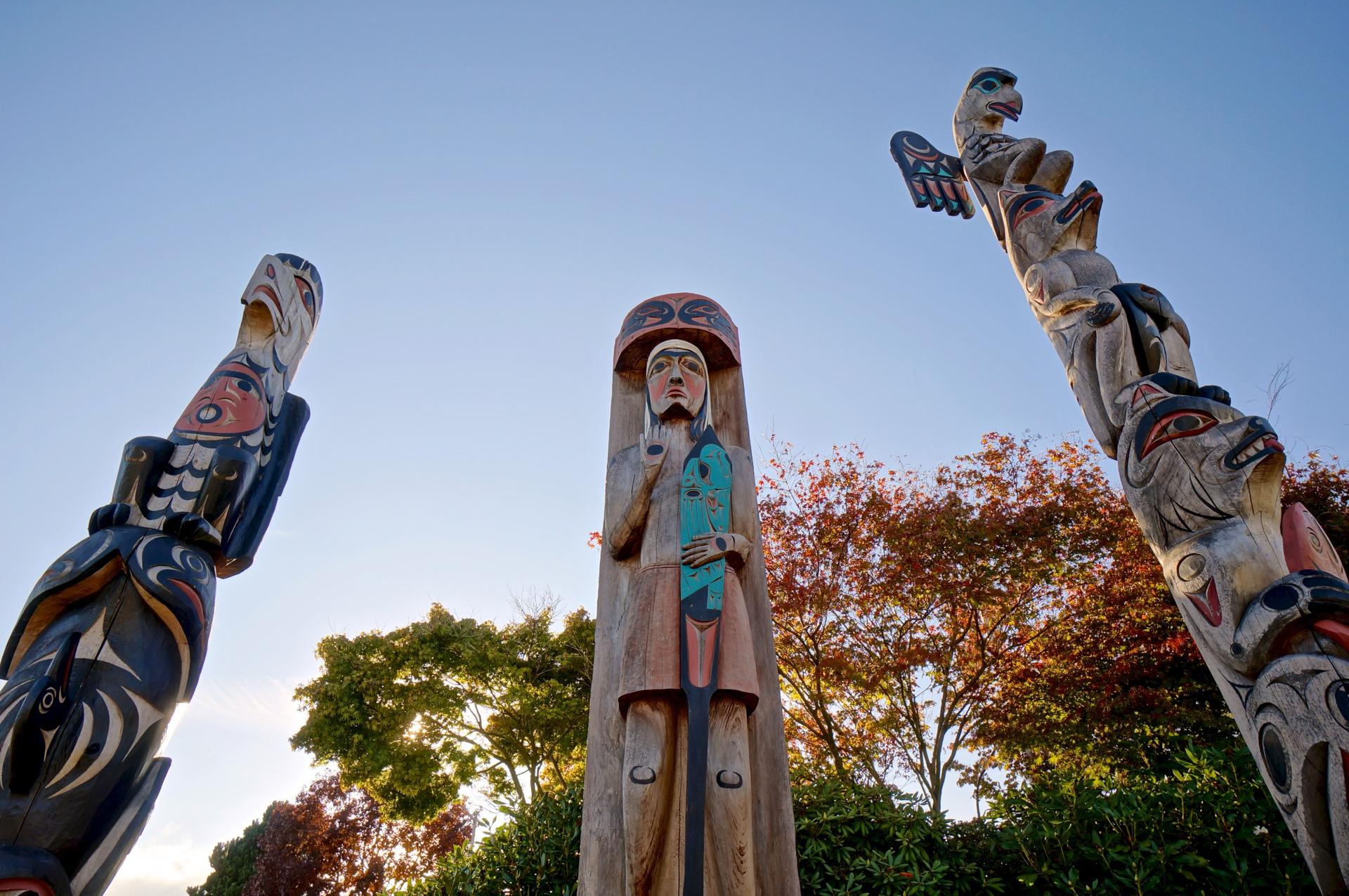Orca & Thunderbird
This totem depicts one of the most important historical legends in Coast Salish history.  The Thunderbird seen on the tail of the orca is a spiritual being and can only be accessed through communication with the creator.  It is usually a plea for help.
The orca is the most respected creature of the sea.  It is held in very high respect by Coast Salish people because of its physical powers and superior intellect.  They survive in packs like wolves and are sometimes designated in the same realm as wolves of the sea.
A coming together of thegreat spiritual power and awesome physical power can be seen as a balance of power beneficial to mankind as seen through First Nations beliefs.
Salish Welcome Figure
In the past, human figures were carved in much greter than life size.  They stood in front of villages with hands and arm held in a welcome gesture.
This welcome figure is based on a traditional Coast Salish welcome figure that would have been seen in front of villages.  They faced the water and welcomed arriving visitors.  The hands and arms of this figure shows the welcome gesture as well as an arm holding a paddle, showing that the people of the First Nation from Saanich are people of the canoe and paddle.  These are symbols of welcome and thanks as well as survival.
Raven, Wolf, and Bear
This totem is a depiction of a bird and animals held in high esteem bu the Saanich people.  In the days of the past, when forests, oceans, rivers and streams were in pristine condition, animals, birds, sea creatures, and mankind of the Saanich First Nations held a close relationship to each other.  They shared the space provided by our creator "XAIES"; along with a closer understanding and respect between mankind, our brothers and sisters, and other life forms which we believe we are a part of.
On this pole the Raven sits atop the head of the Wolf and below the Wolf is the Bear clutching a salmon.  The Raven is Saanich mythology is noted for its intelligence and is regarded as a messenger as it flies its daily path across the sky, waters, forests, and villages spreading the news of the day.  This intelligent bird loves to play tricks on all including mankind as it makes its daily journey.  In many First Nations culturs the Raven is acknowledged for its ability to transform into other deities further enhancing its reputation as the trickster and messenger.
The second figure under the Raven is the Wolf. The Wolf at one time inhabited this ground and surrounding areas.  Wolves were regarded as keepers of the night and could be heard talking to each other over great distances.  They were regarded as protectors and guarded our sacred places such as the top of Mt. Newton - a place reserved for survival of such things as the great flood as well as our place for meditation, purification, and fasting and coldwater rituals.  Wolf packs and Orca pods are revered by First Nations as one and the same.
The Bear on the bottom of this pole is holding a salmon to show that he or she is also a fisherman and survivor.  Bears are respected and regarded as our equal as family caretakers and will rigourously defend their young as does man.  Bears are respected as people and can be seen fishing in close proximity to our fisherman in the shallows of rivers as the salmon journey upstream.  We have a saying which says, "salmon for survival are survival for salmon."  Bears believe this as do we and we have a mutual respect for each in this regard.
Charles W. Elliott is an internationally recognized Master Carver and fine artist in the Coast Salish tradition.  His art works are in private and corporate collections worldwide.  Charles is a member of the T'sartlip First Nation and was born on the T'sartlip Reserve in Brentwood Bay, BC.  He continues to live there today on the shores of the Saanich Inlet with his wife Myrna and their children.
As a young artist, Charles carved designs on the bark of the cottonwood tr