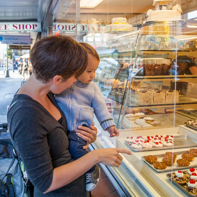 Woman holding child outside The Dutch Bakery looking at pasteries