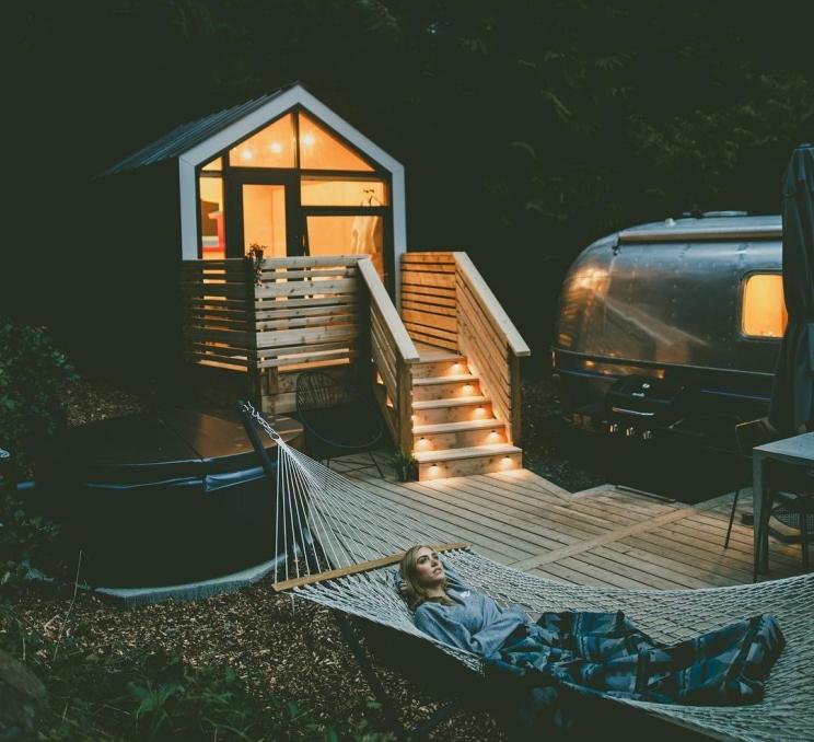 A woman relaxing in a hammock next to an Airstream trailer and cabin at night