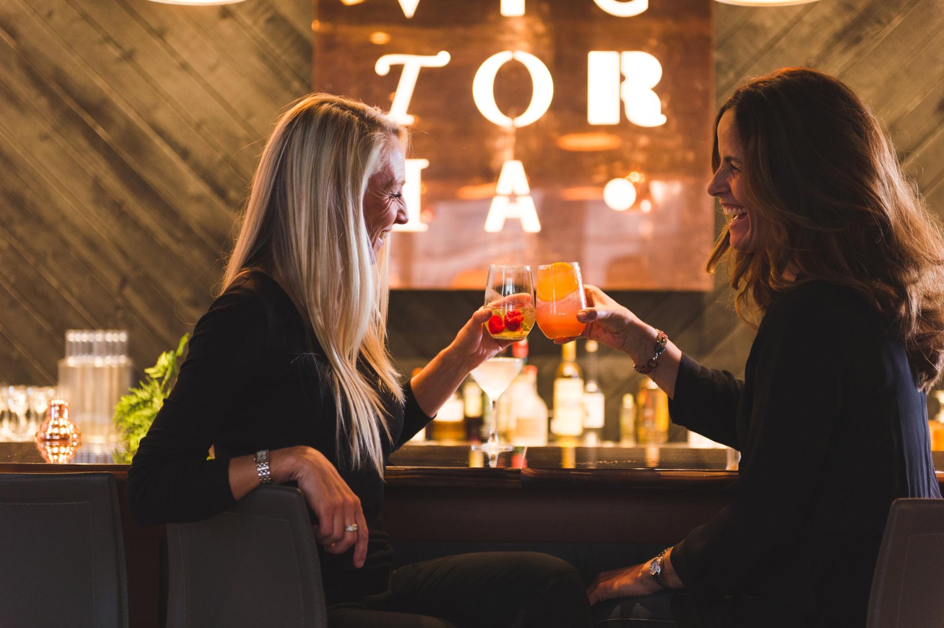 Two women cheersing colourful cocktails at Victoria Distillers