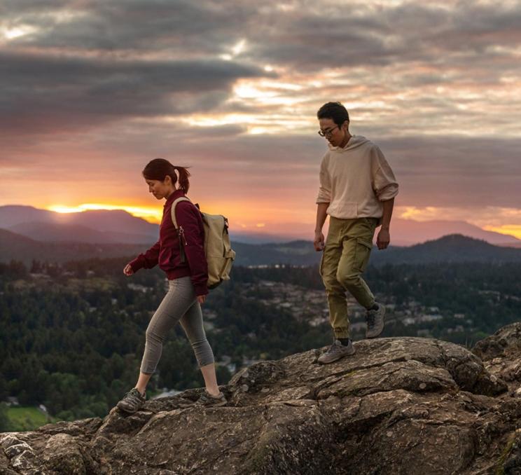 A couple walks along a ridgeline at sunset at PKOLS (formerly Mount Douglas regional park) in Victoria, BC