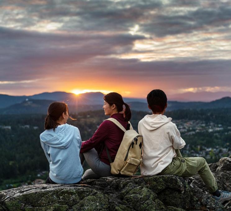 A family sits atop PKOLS (formerly Mount Douglas) regional park, after a hike, in Victoria, BC