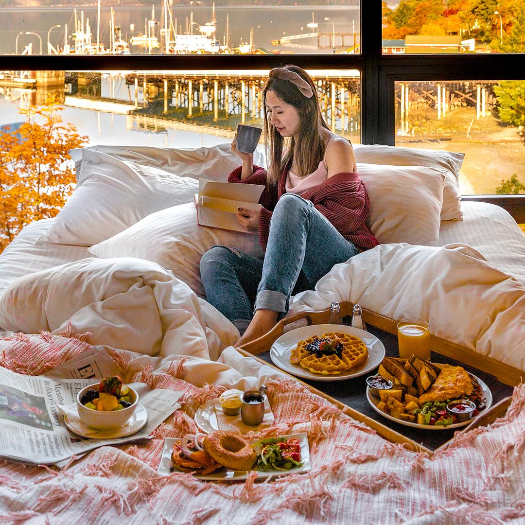 A woman enjoys a large spread of breakfast in bed at a Victoria, BC hotel