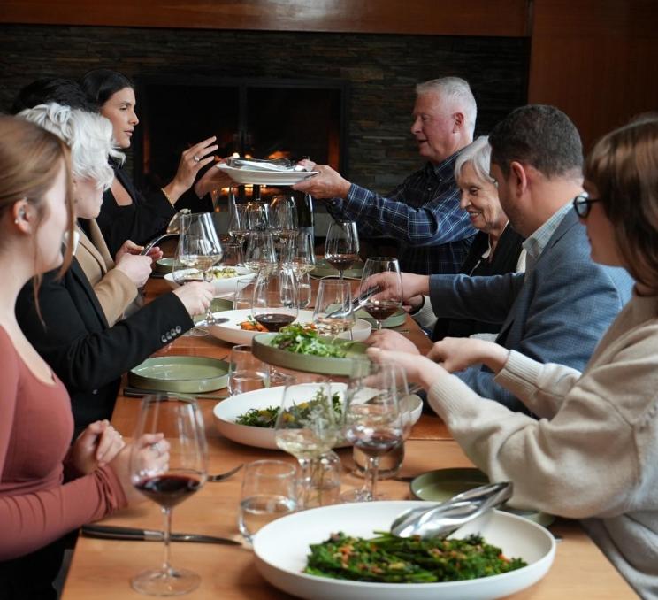 Guests gathered around a communal dining table enjoying a chef-prepared meal with wine.