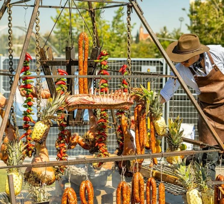 Open-fire cooking display featuring hanging meats, sausages, peppers, and pineapples at Brewery & the Beast.