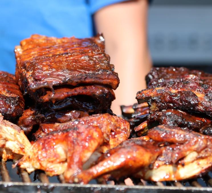 Barbecued ribs and chicken grilling over an open flame at a food festival.