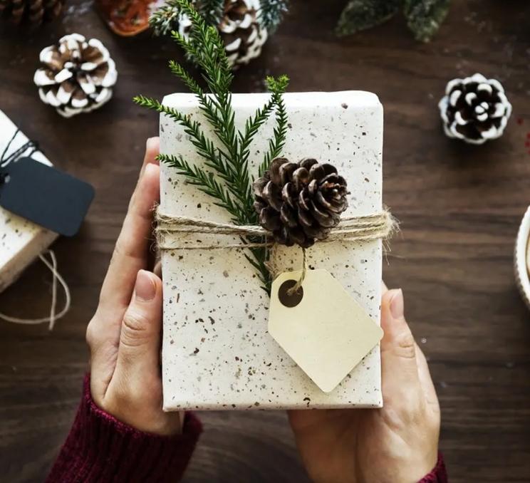A woman holds a wrapped Christmas box adorned with a pinecone