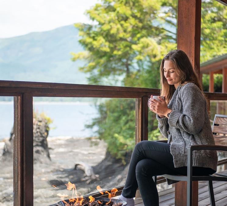 A woman enjoys a cozy cup of coffee, fireside, at Wild Renfrew just outside of Victoria, BC