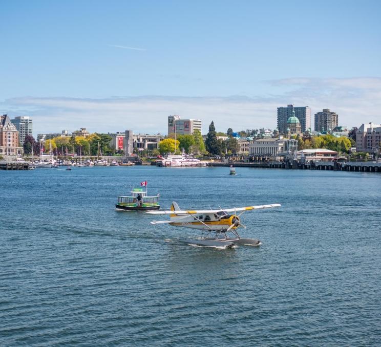 A Kenmore Air seaplane flight taxis across Victoria's Innner Harbour, while a Victoria Harbour Ferry passes in the background, in Victoria, BC
