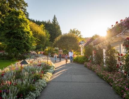 A family walks hand-in-hand along a flowered pathway at The Butchart Gardens, a National Historic Site of Canada, in Victoria, BC