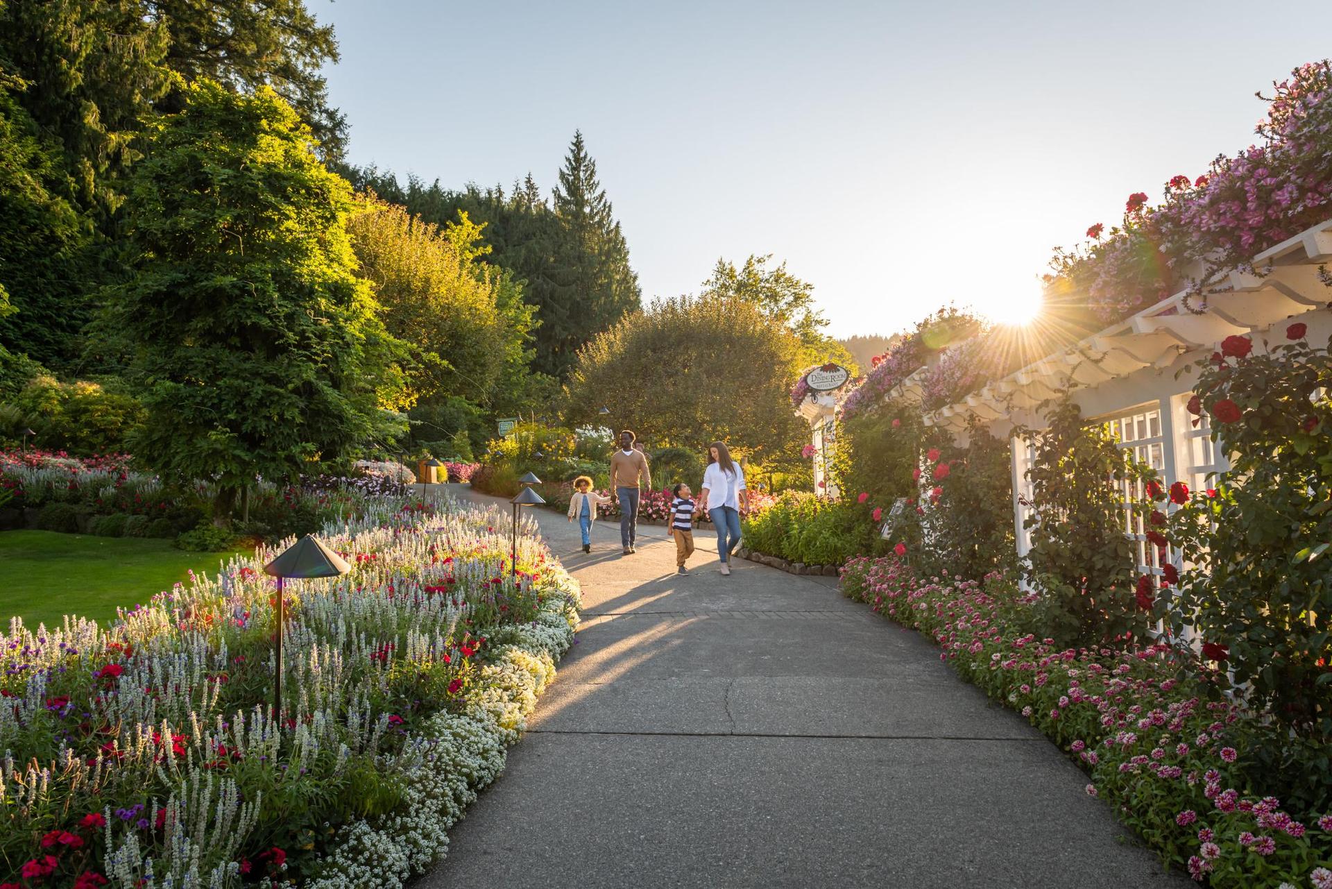 A family walks hand-in-hand along a flowered pathway at The Butchart Gardens, a National Historic Site of Canada, in Victoria, BC