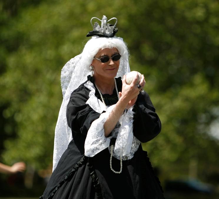 A person in a Victorian era dress plays softball during Victoria Pride Week in Victoria, BC