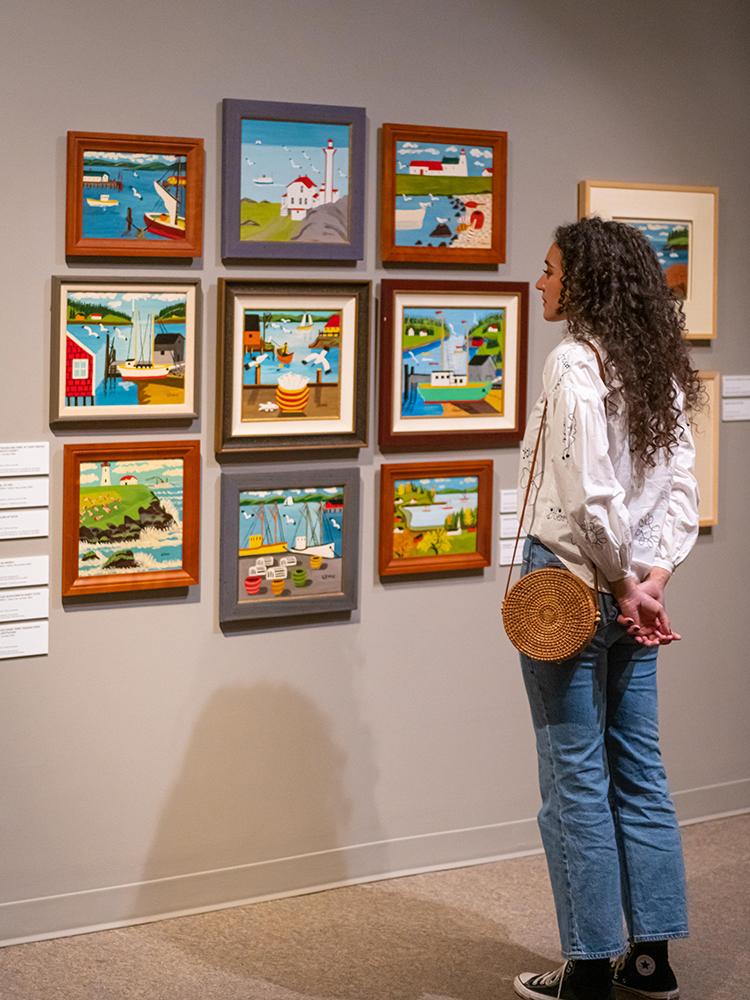 A woman in a white shirt examines art by Maude Lewis at the Art Gallery of Greater Victoria, in Victoria, BC