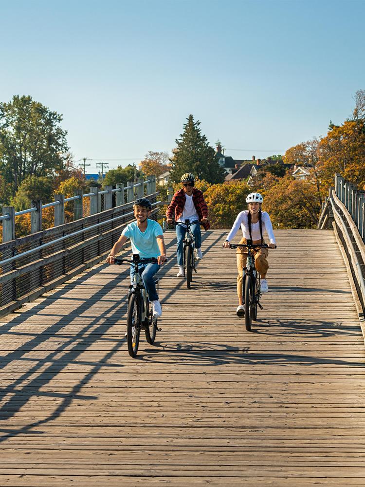 Three friends ride bikes over the Selkirk Trestle on the Galloping Goose Regional Trail in Victoria, BC on a fall day