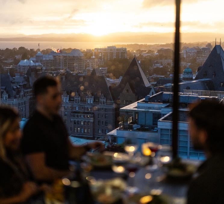 A group dines at Vista 18, a rooftop restaurant in the Chateau Victoria Hotel & Suites, as the sun sets in Victoria, BC