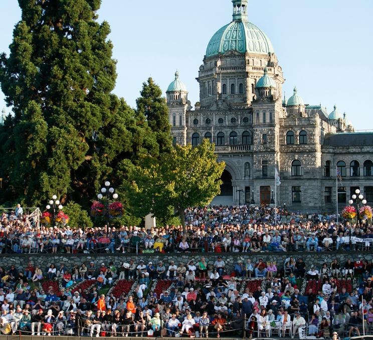A crowd gathers along the Inner Harbour across from the BC Parliament Buildings to watch Symphony Splash! in Victoria, BC
