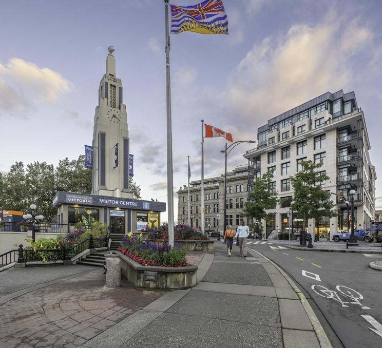 A woman in a pink top and a man in a blue sweater walk past the Victoria Visitor Centre in Victoria, BC