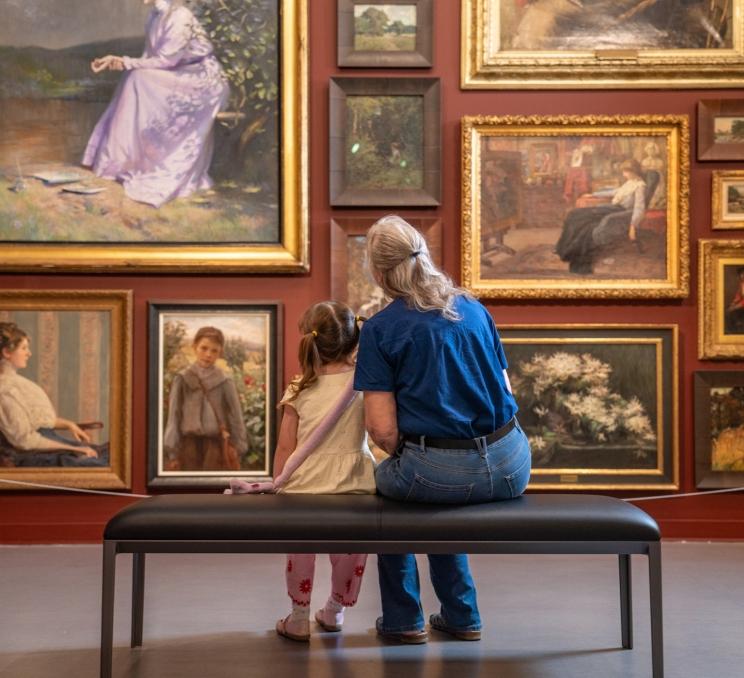 An adult and child view a collection of framed paintings at the Art Gallery of Greater Victoria.
