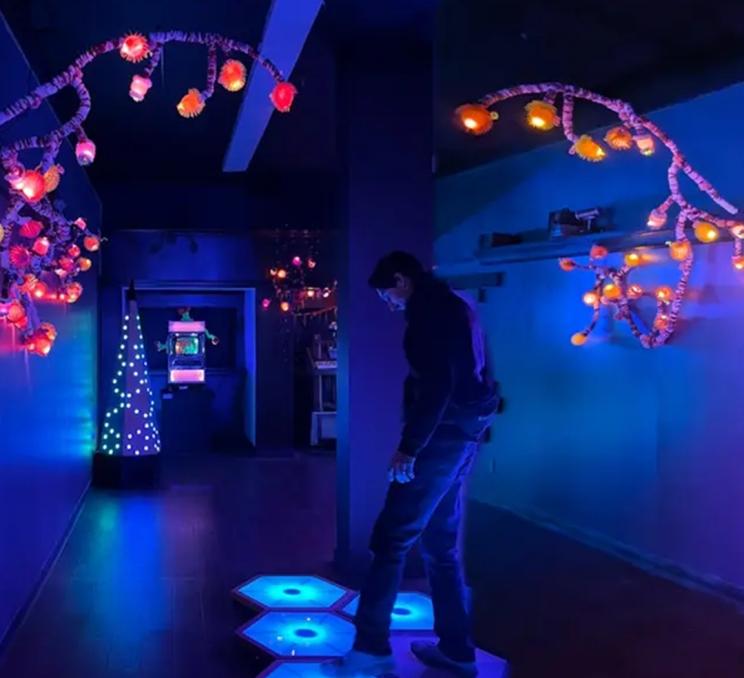 A person steps on illuminated tiles in a hallway at Monkey C Artcade in Victoria, BC