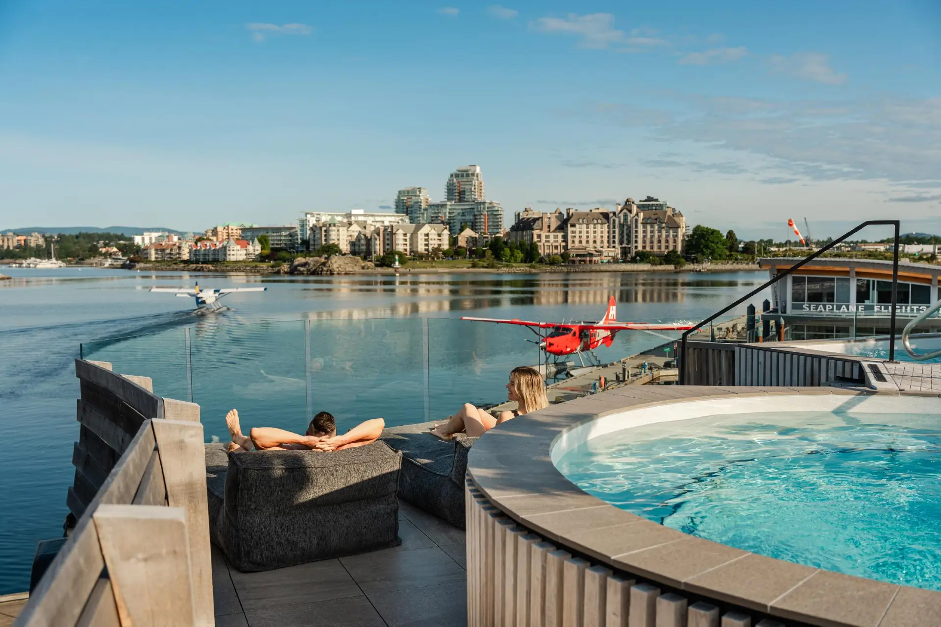 A couple lounges in the sunshine on the deck at HAVN Saunas watching the seaplanes on the Inner Harbour in Victoria, BC