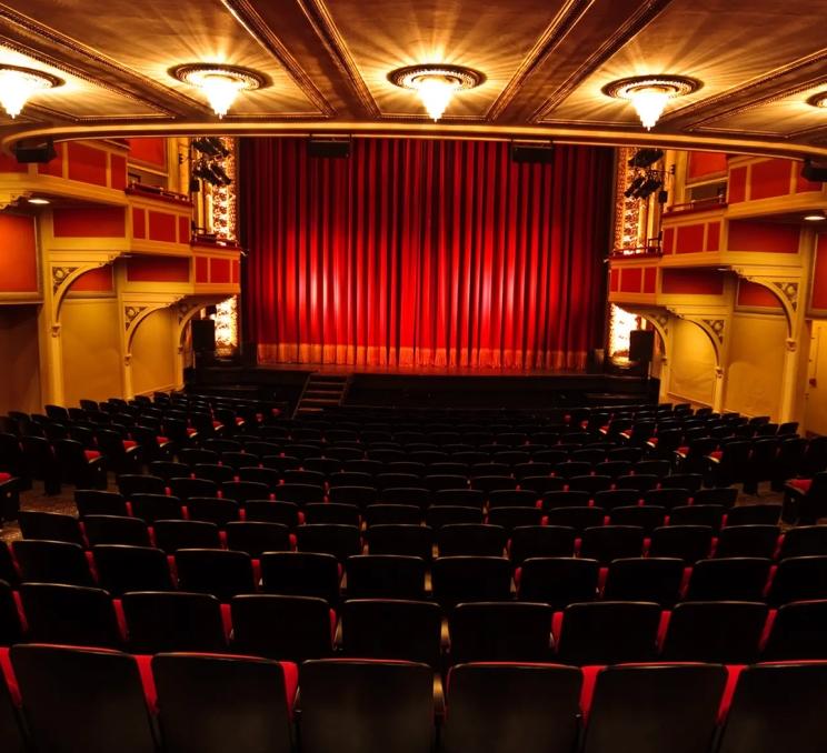Interior of the Royal Theatre in Victoria, featuring rows of seating, ornate architectural details and a red-curtained stage.