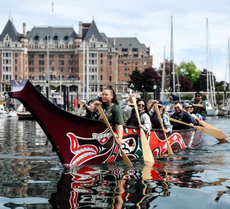 A Songhees Tour group paddles a decorated canoe through Victoria’s Inner Harbour