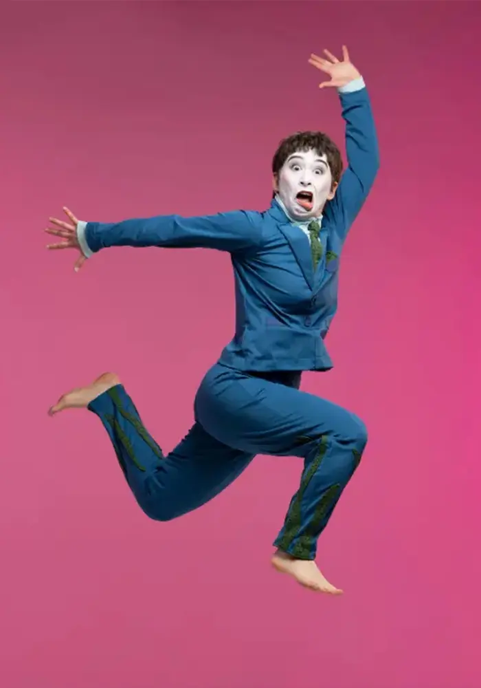 A mime jumps through the air in front of a purple back drop