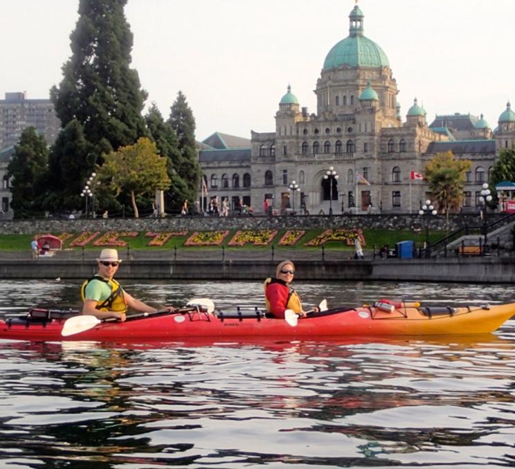 A couple paddles kayaks past the BC Parliament Buildings on the Inner Harbour of Victoria, BC