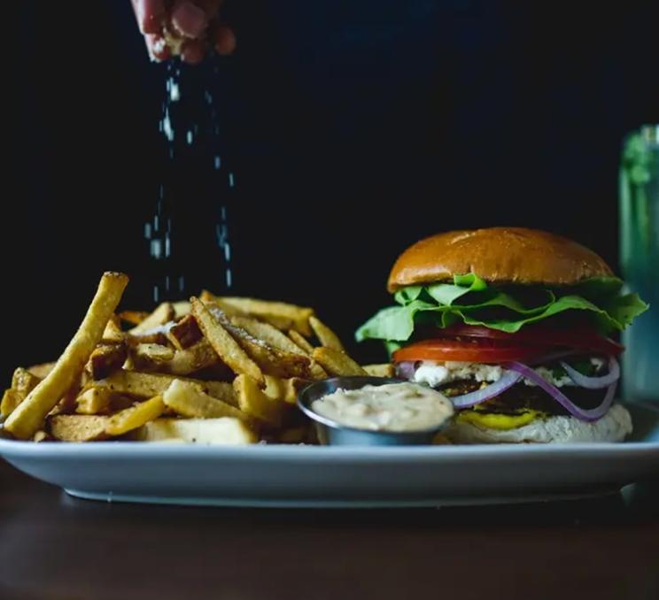 A chef season's the fries on a plate with a burger at Bin 4 Burger Lounge in Victoria, BC